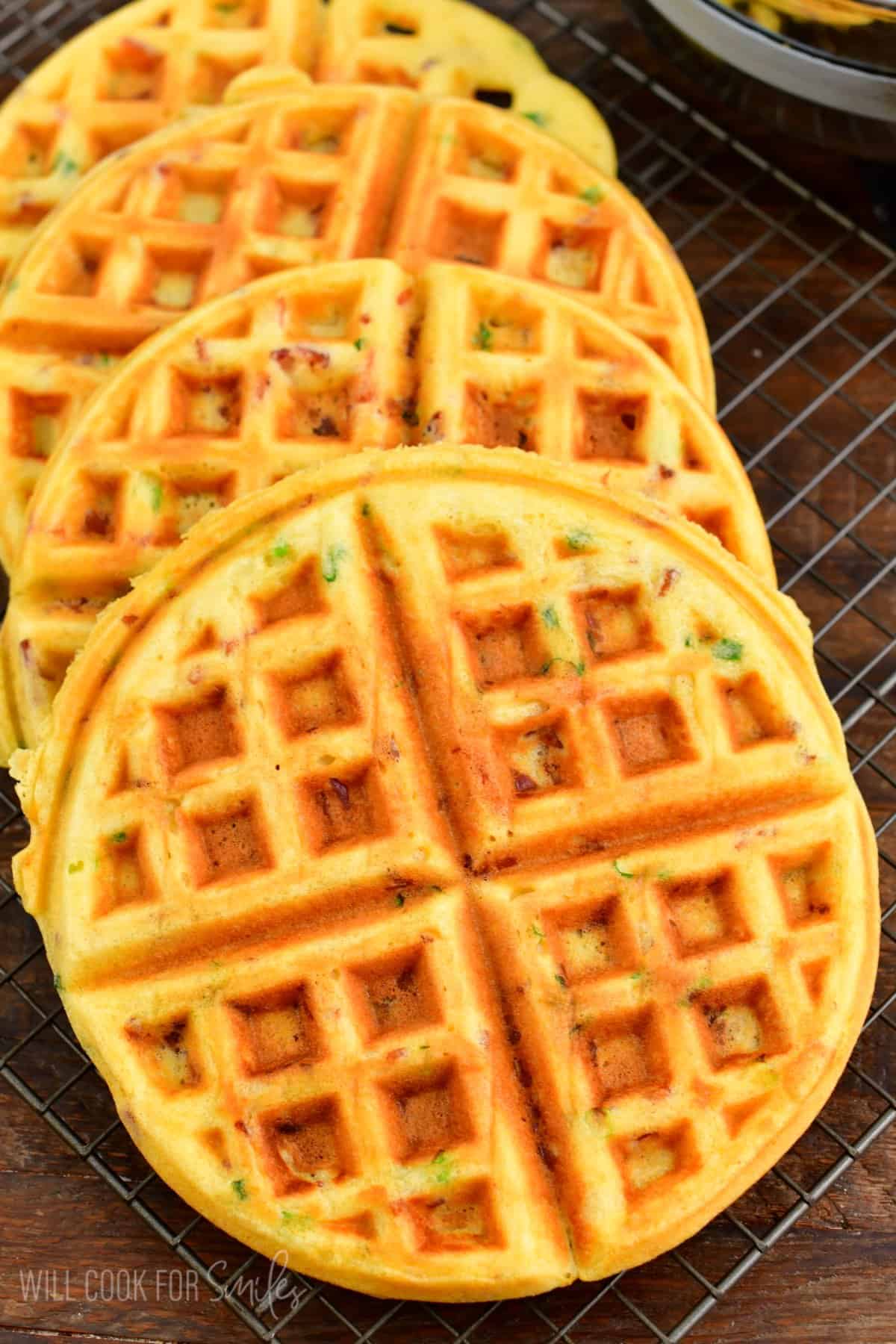 four cooked savory waffles on a wire rack on a wood surface.