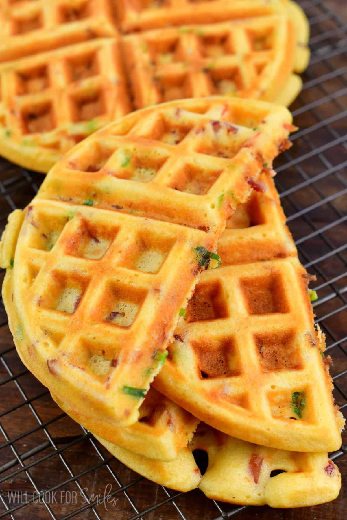 Savory waffles cut in half on wire rack on top of a wood surface.