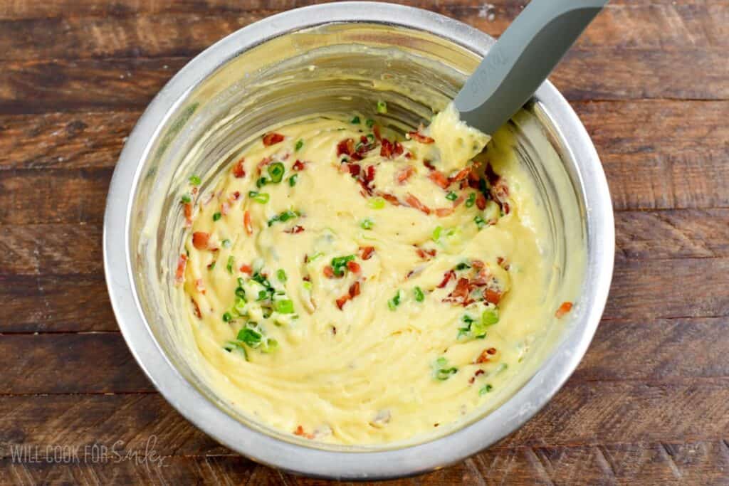 folding ingredients into waffle batter that is in a bowl on a wood surface.