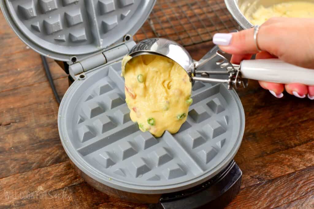 Using an ice cream scoop to scoop waffle batter into waffle maker.
