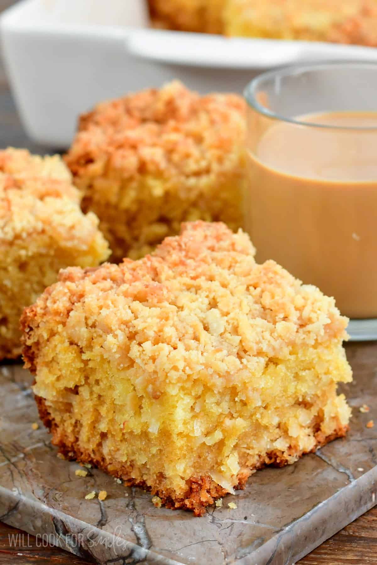 Slice of coconut coffee cake with a glass of coffee next to it.