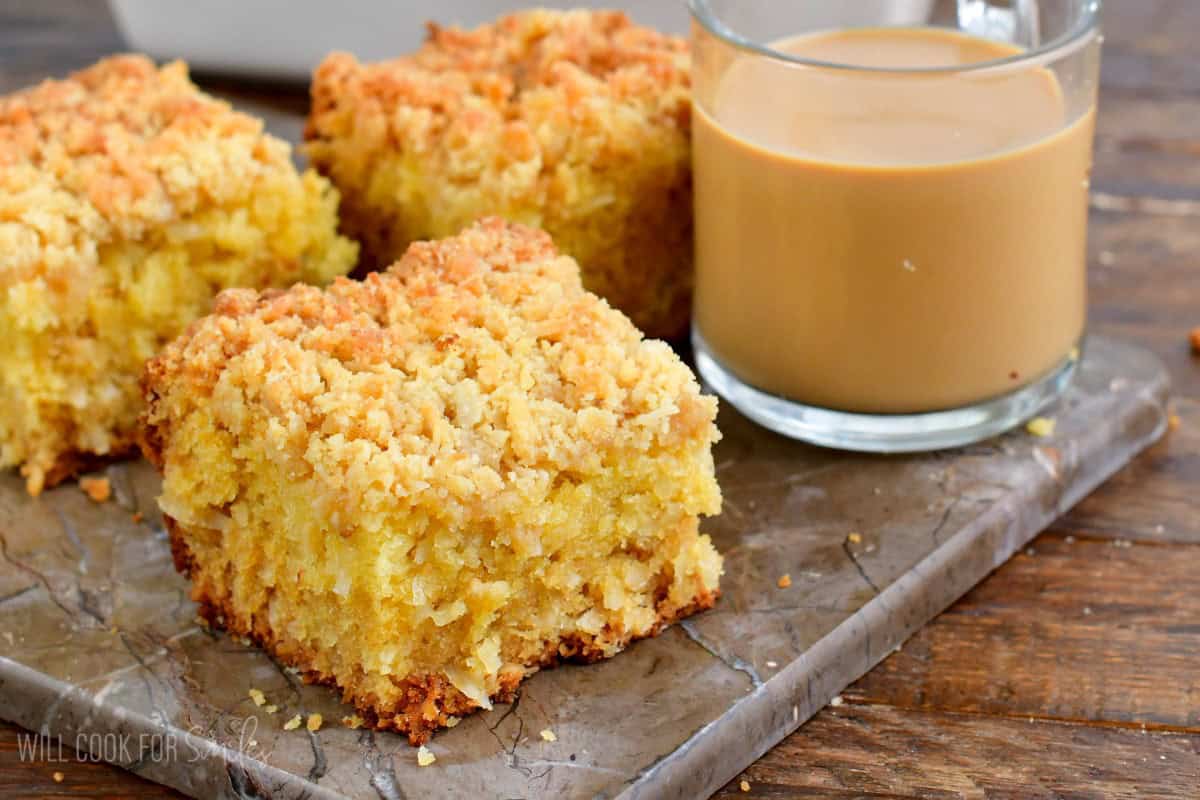 three slices of coconut coffee cake with a glass mug of coffee on a piece of marble.