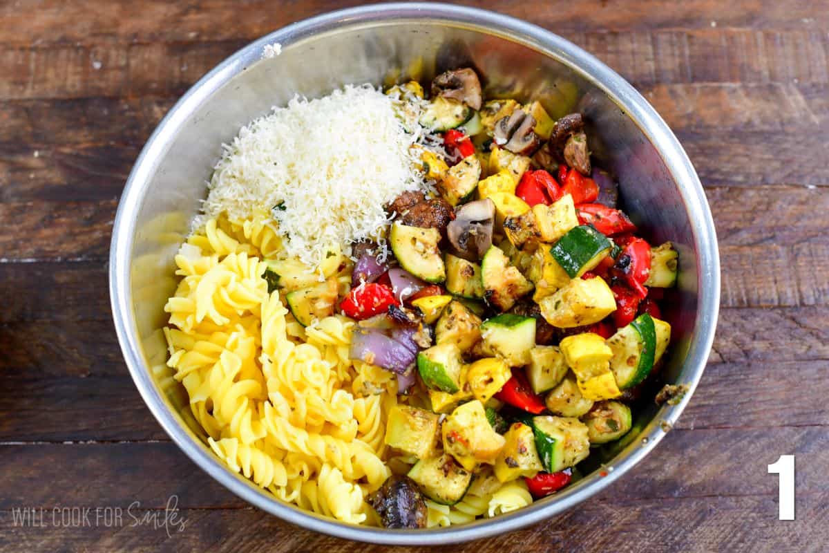 Grilled vegetable pasta salad ingredients in a metal bowl on a wood surface.