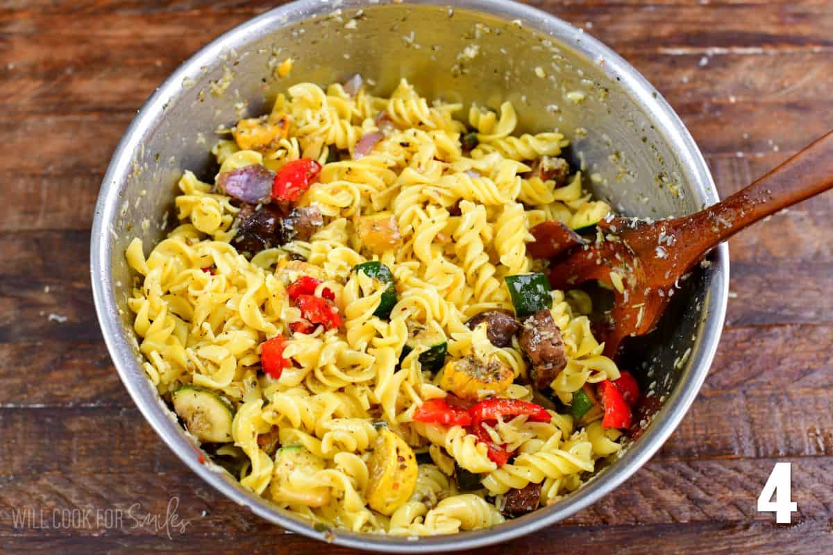 Mixing the ingredients in a bowl with a wooden spoon for grilled vegetable pasta salad.