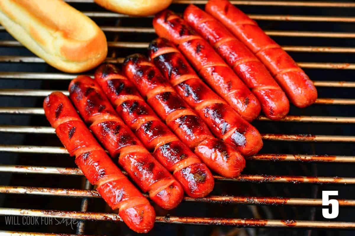 Grilling spiral cut hotdogs next to hot dog buns.