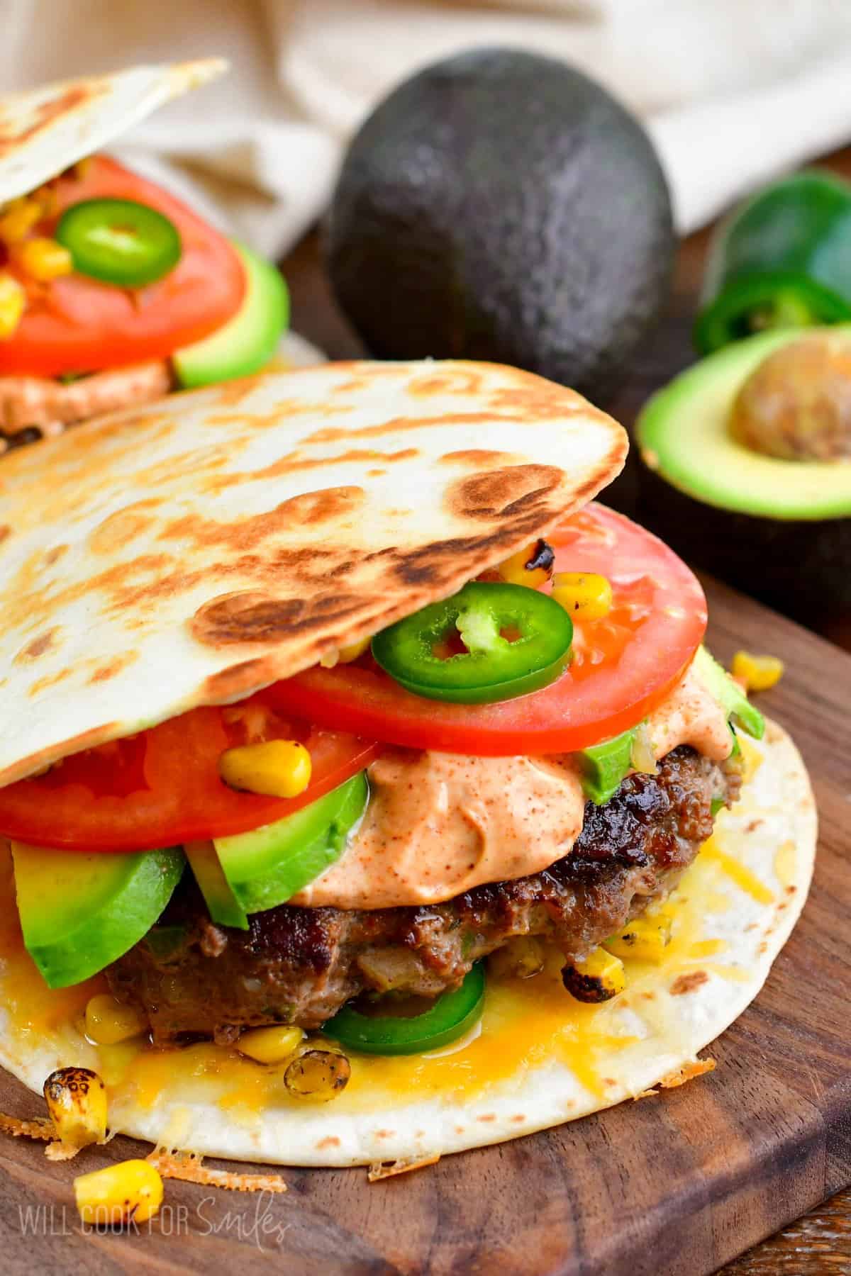 Quesadilla burger with tomato, avocado, and jalapenos on a wood surface.