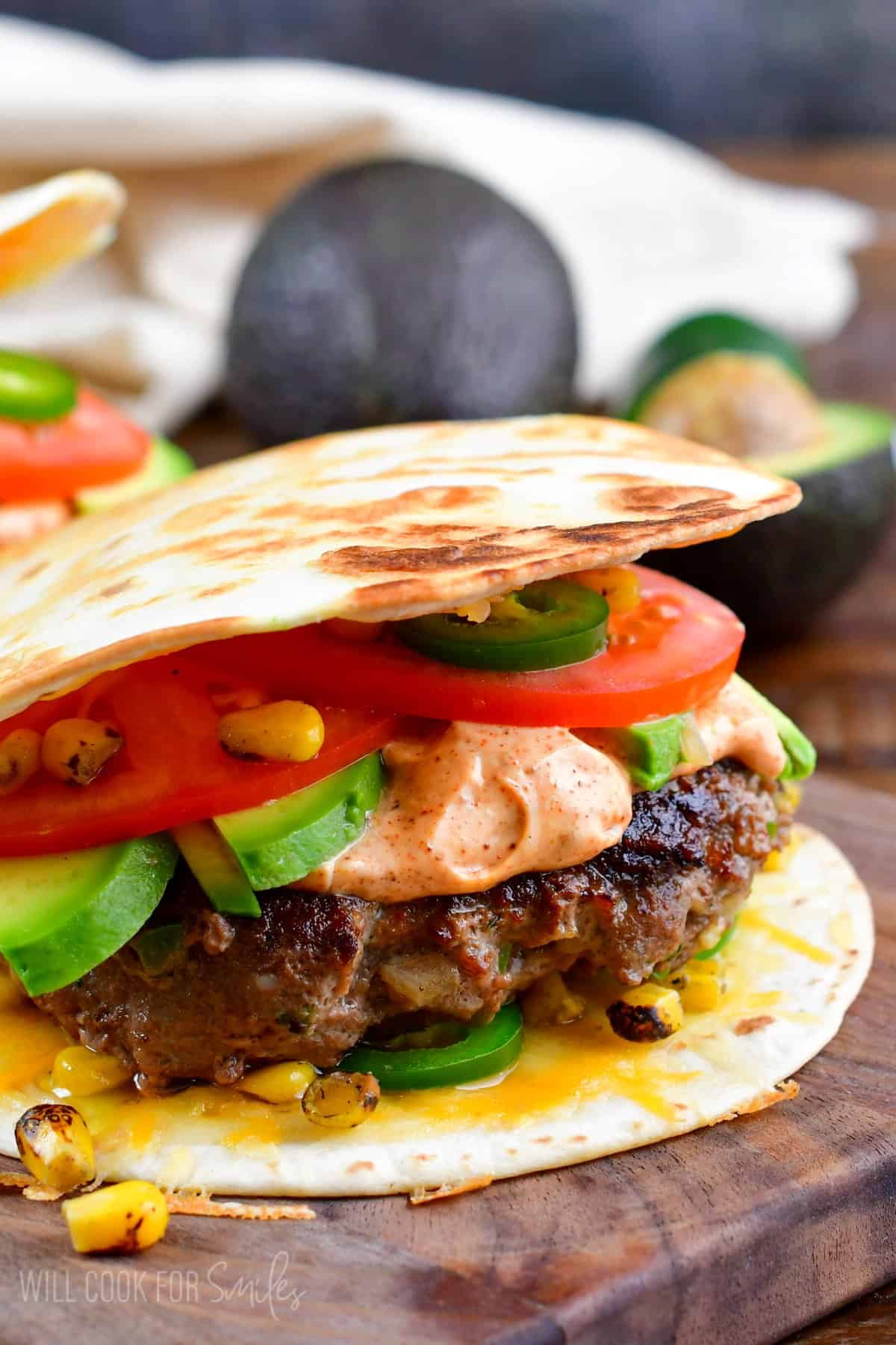 Burger sandwiched between two soft tortillas on a wood surface.