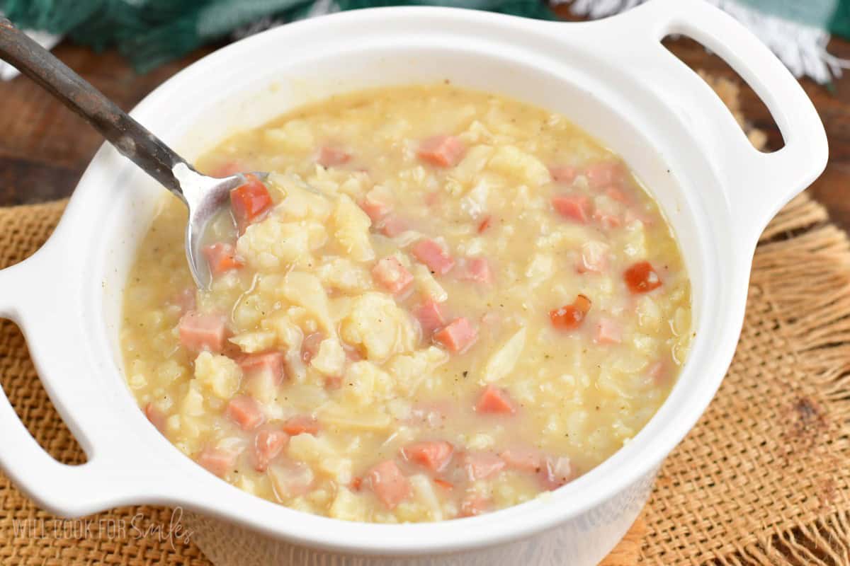 creamy cauliflower soup with ham in a white bowl with a spoon.