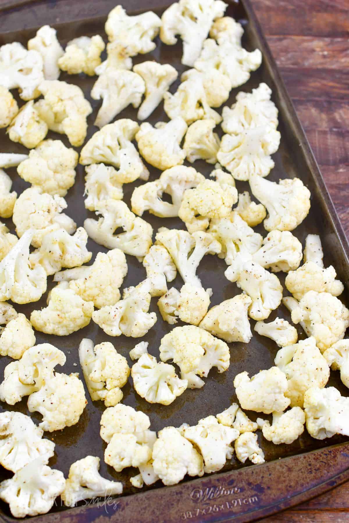 uncooked seasoned cauliflower spread on the baking sheet.