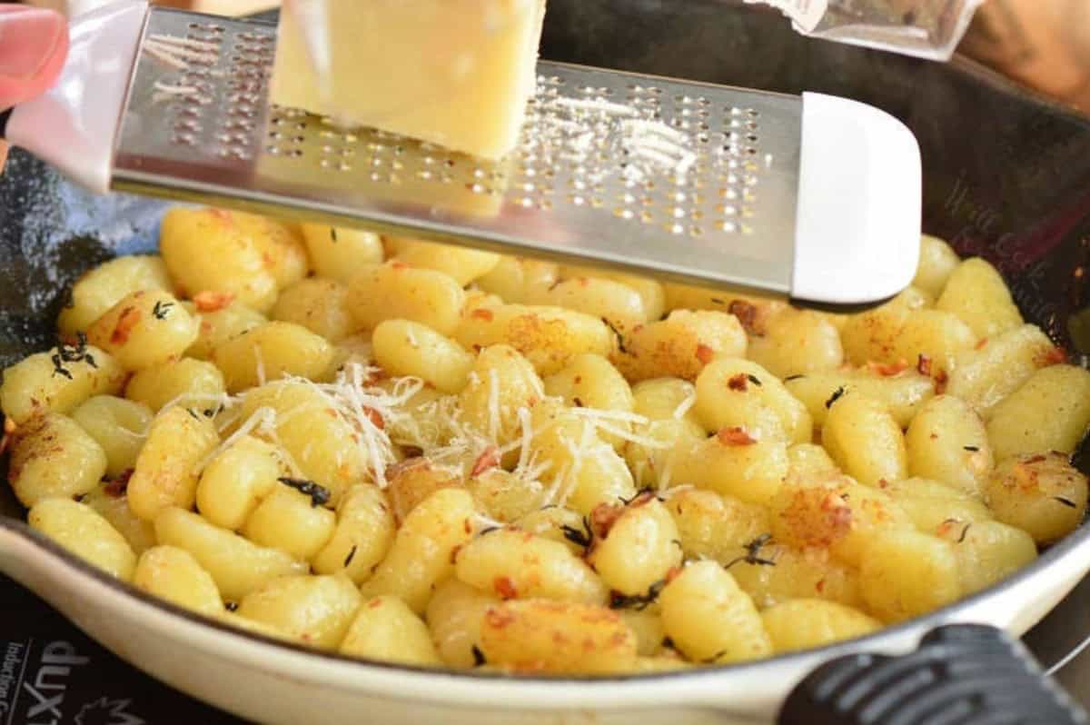grating parmesan cheese over the sauteed gnocchi in the skillet.