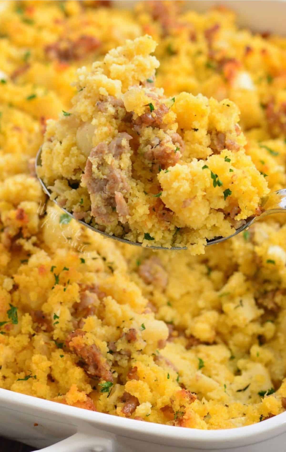 holding a spoonful of cornbread dressing with sausage over the baking dish.