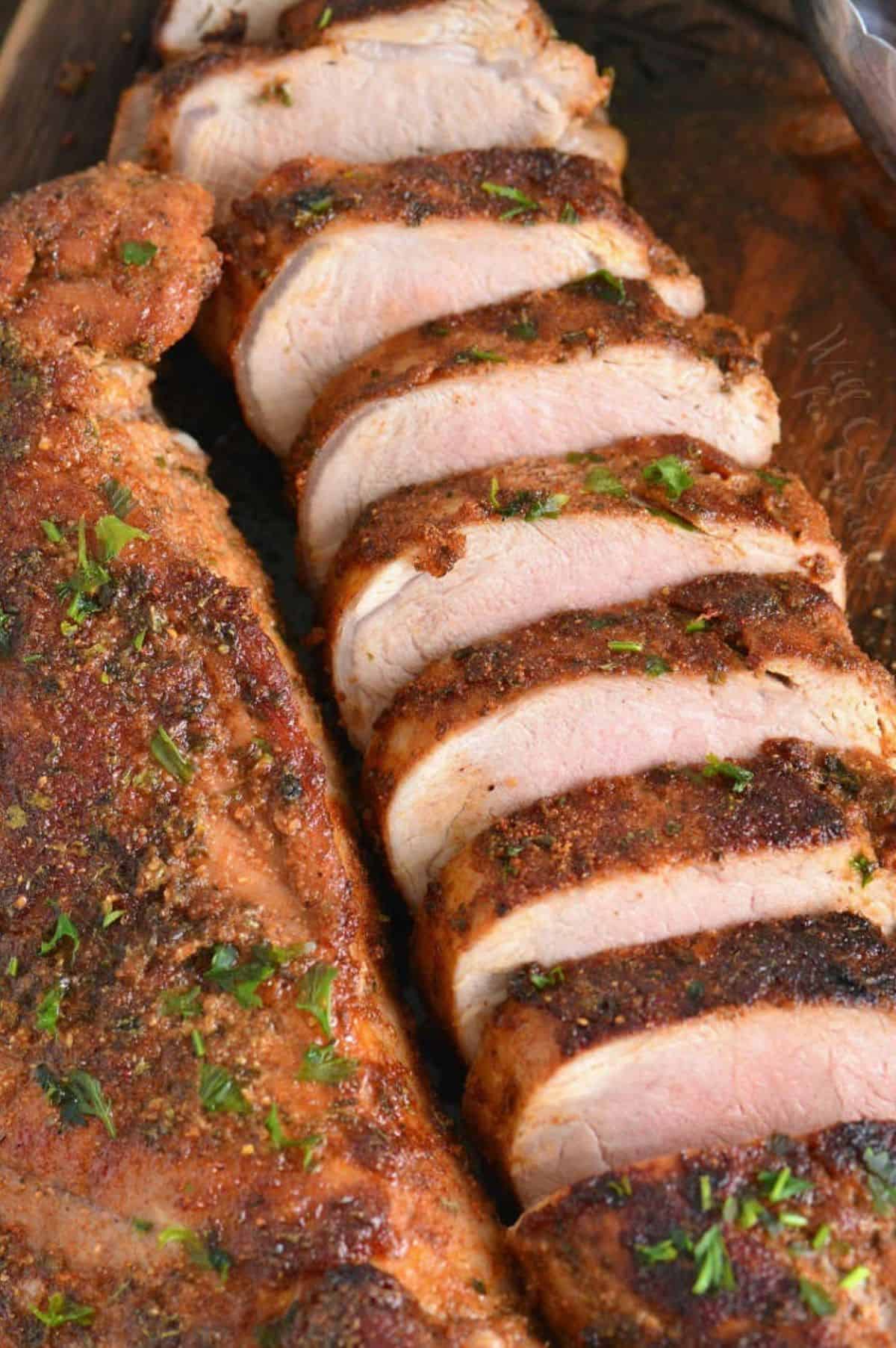 Two sliced roasted pork tenderloin with spice-rub crust and parsley on a wooden platter.