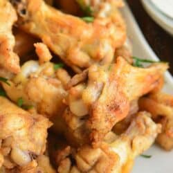 several baked chicken wings on a white plate next to ranch.