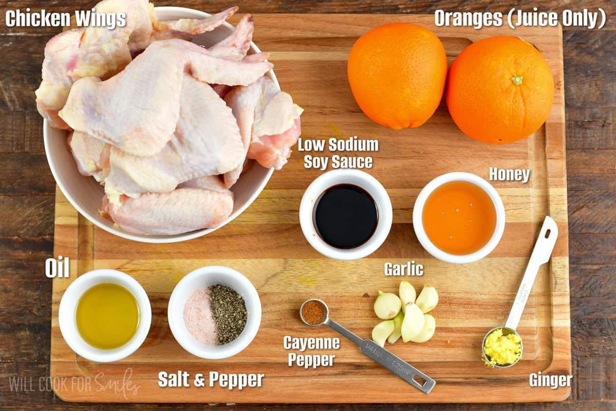 ingredients for orange glazed chicken wings on a wood cuttin board.