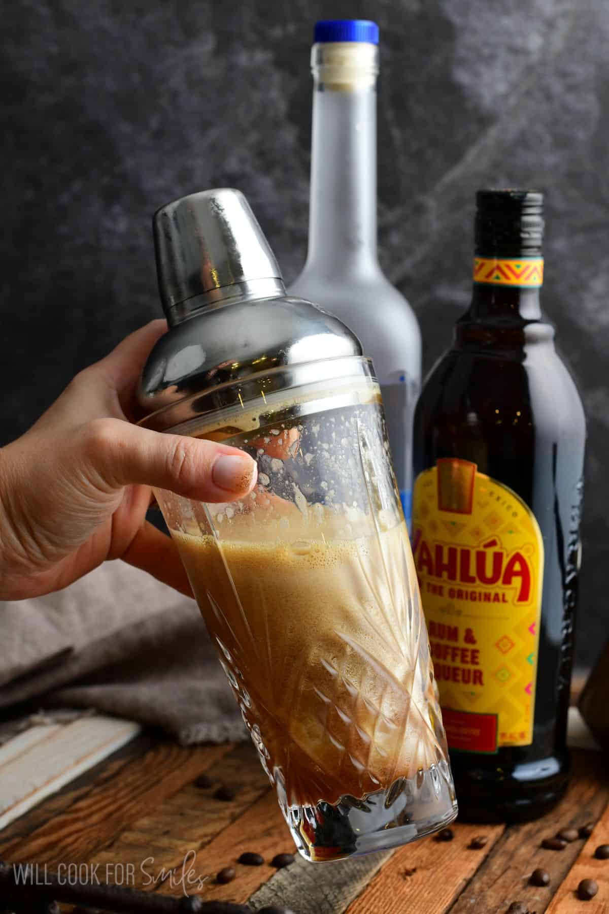holding a cocktail shaker with a well shaken espresso martini in it.