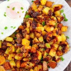 a large side of home fries next to an egg and topped with chives.