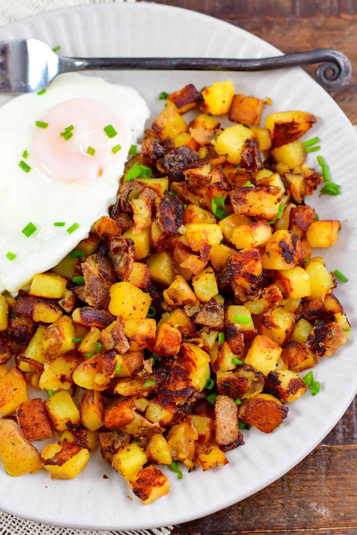 a large side of home fries next to an egg and topped with chives.