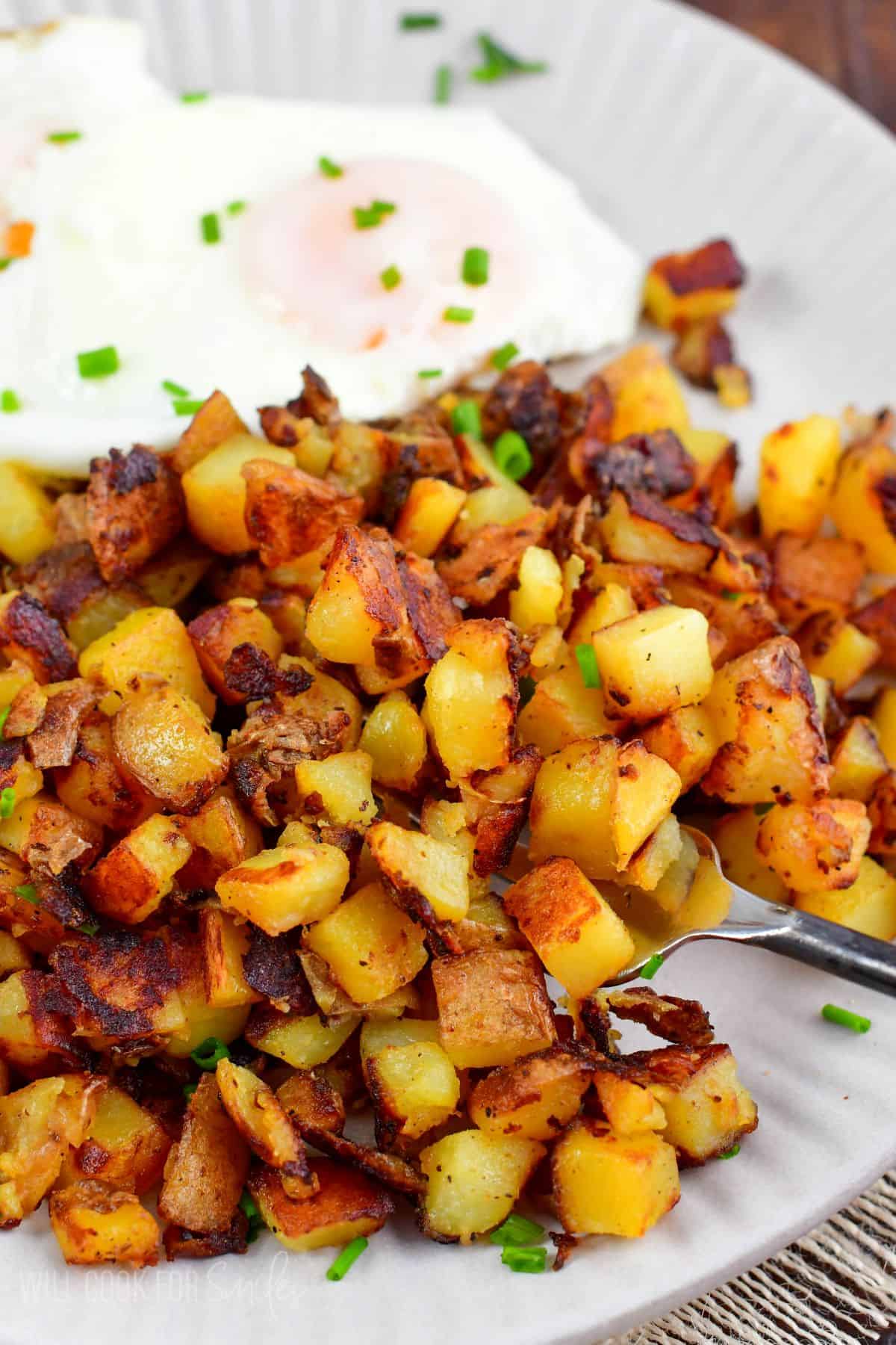 scooping some crispy home fries from the plate using a fork.