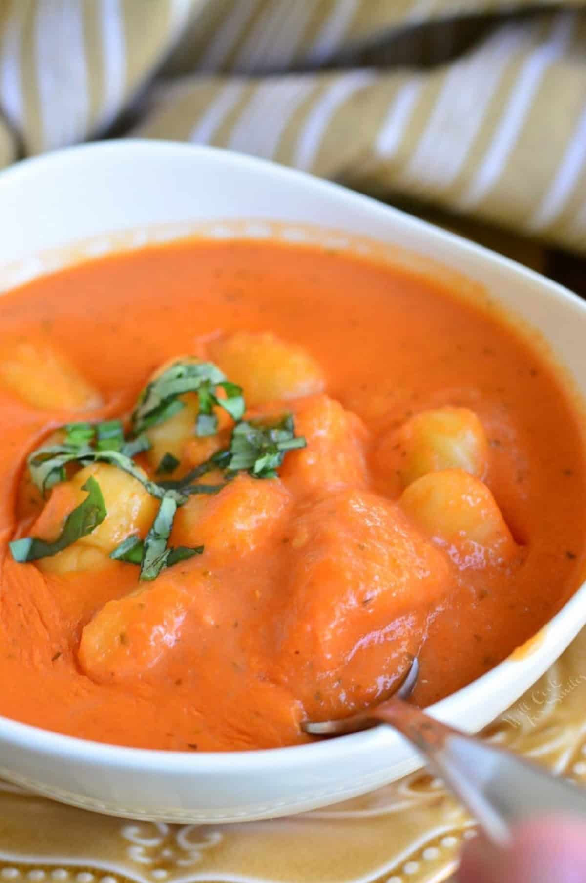 Tomato soup with gnocchi in a bowl with a spoon scooping some out.