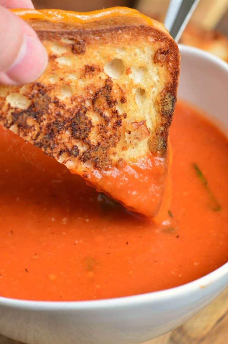 Tomato basil soup in a bowl and dipping in a grilled cheese.