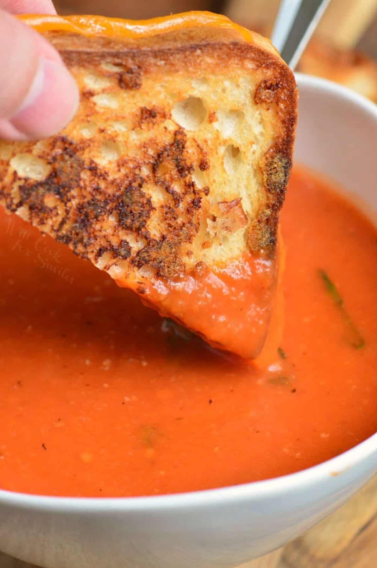 Tomato basil soup in a bowl and dipping in a grilled cheese.