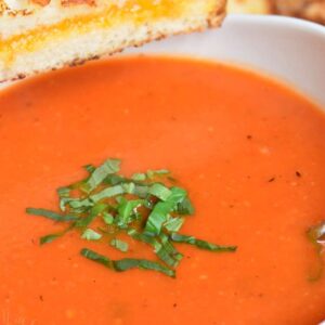 Tomato basil soup in a bowl with basil and with a grilled cheese.