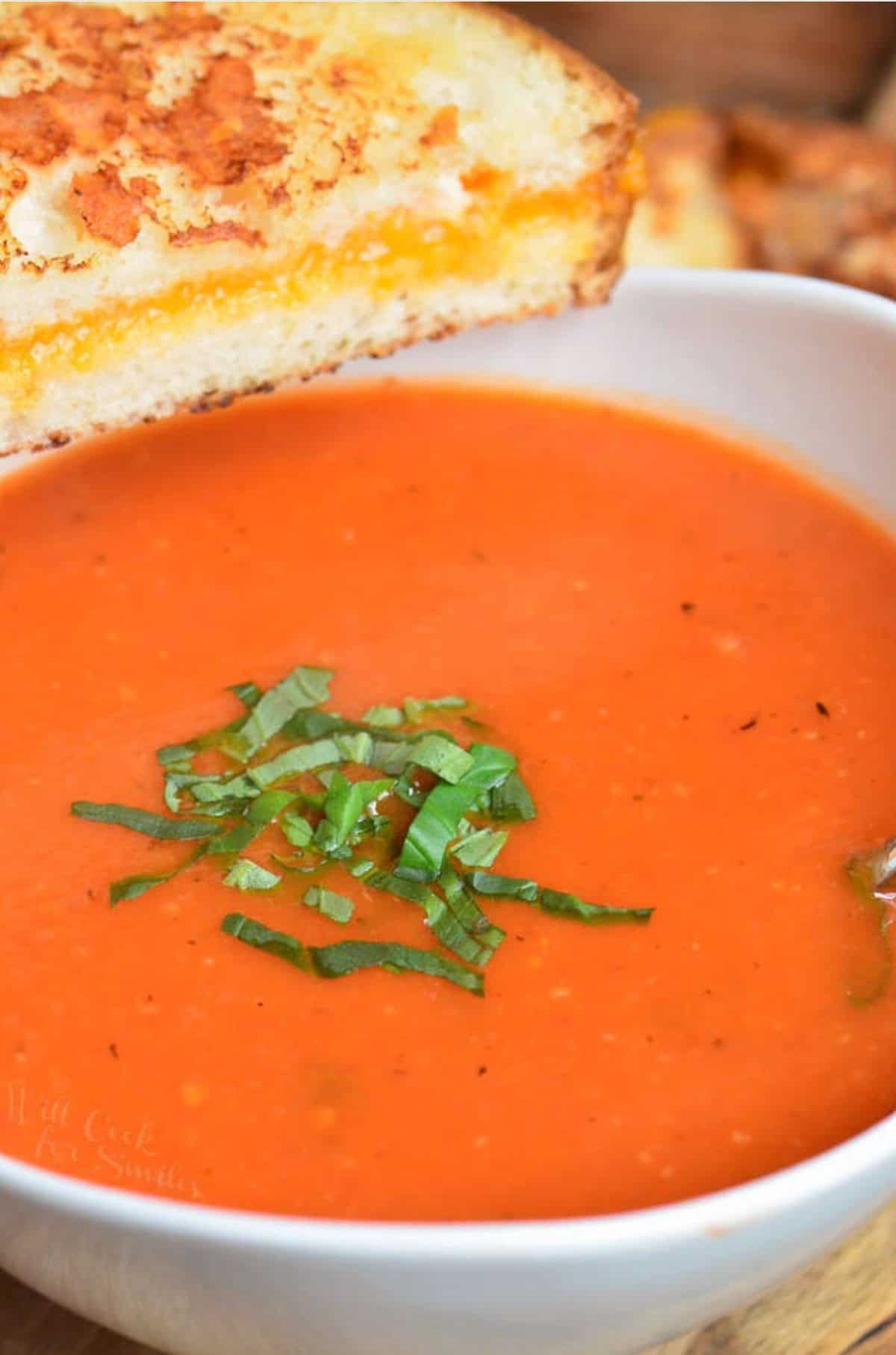 Tomato basil soup in a bowl with basil and with a grilled cheese.