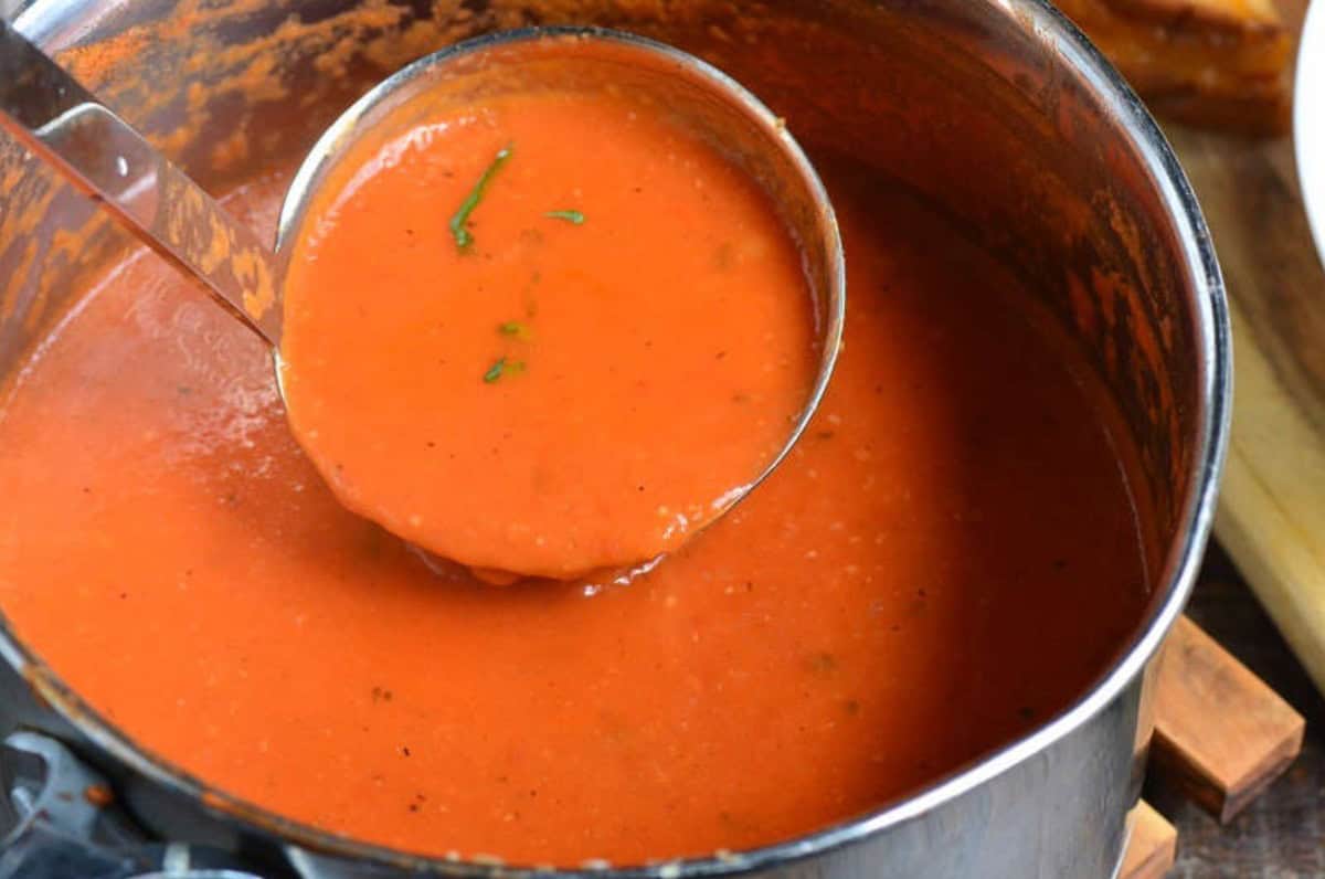 ladeling the tomato basil soup out of a pot.