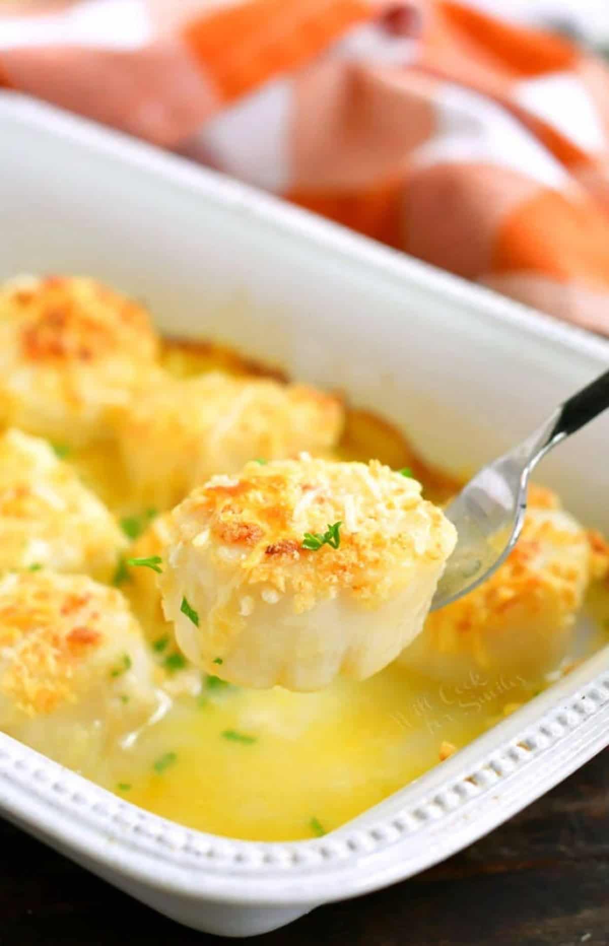 holding one scallop on a fork over the baking dish.