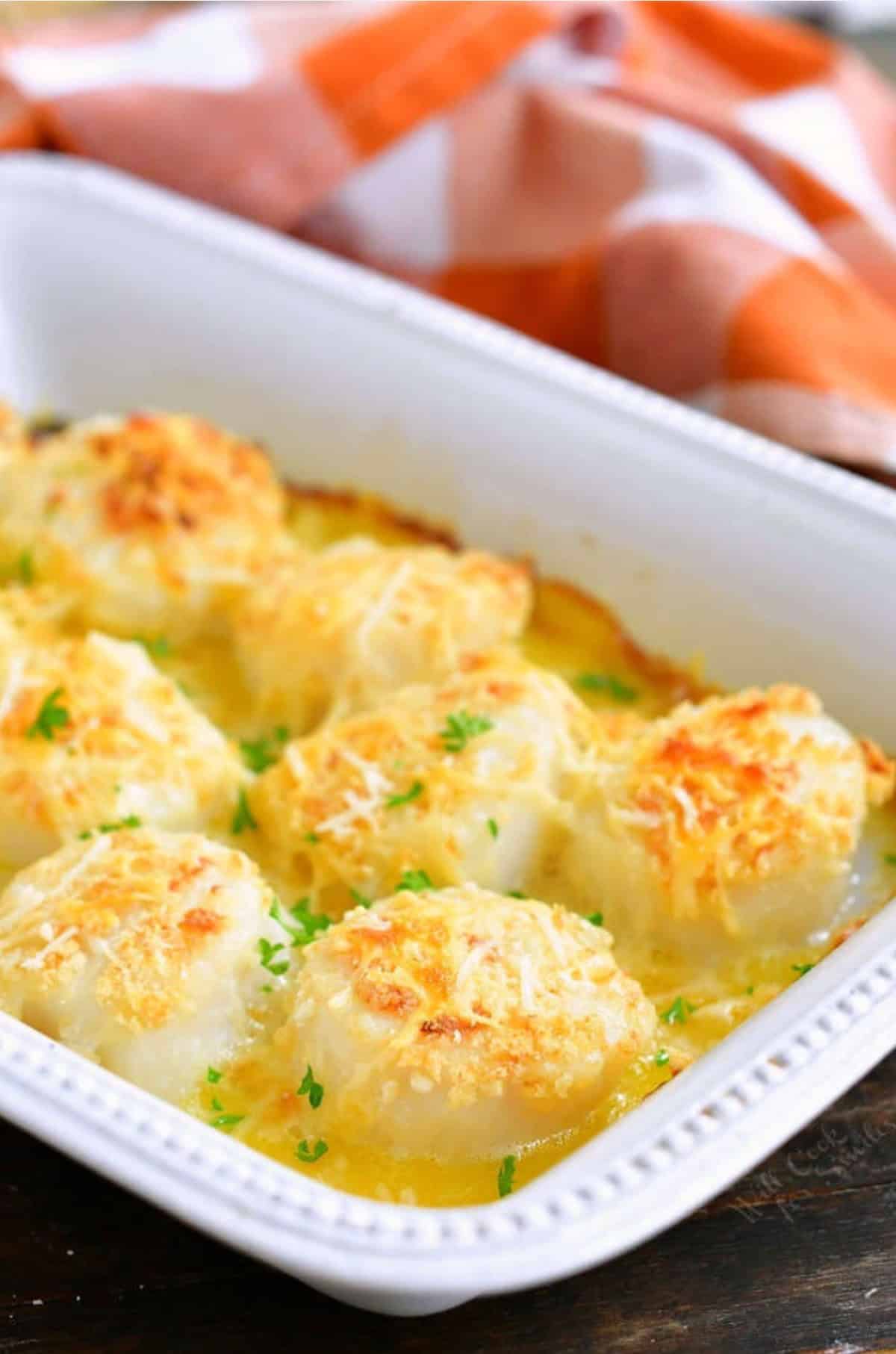 several baked sea scallops in the baking dish with butter and parmesan.
