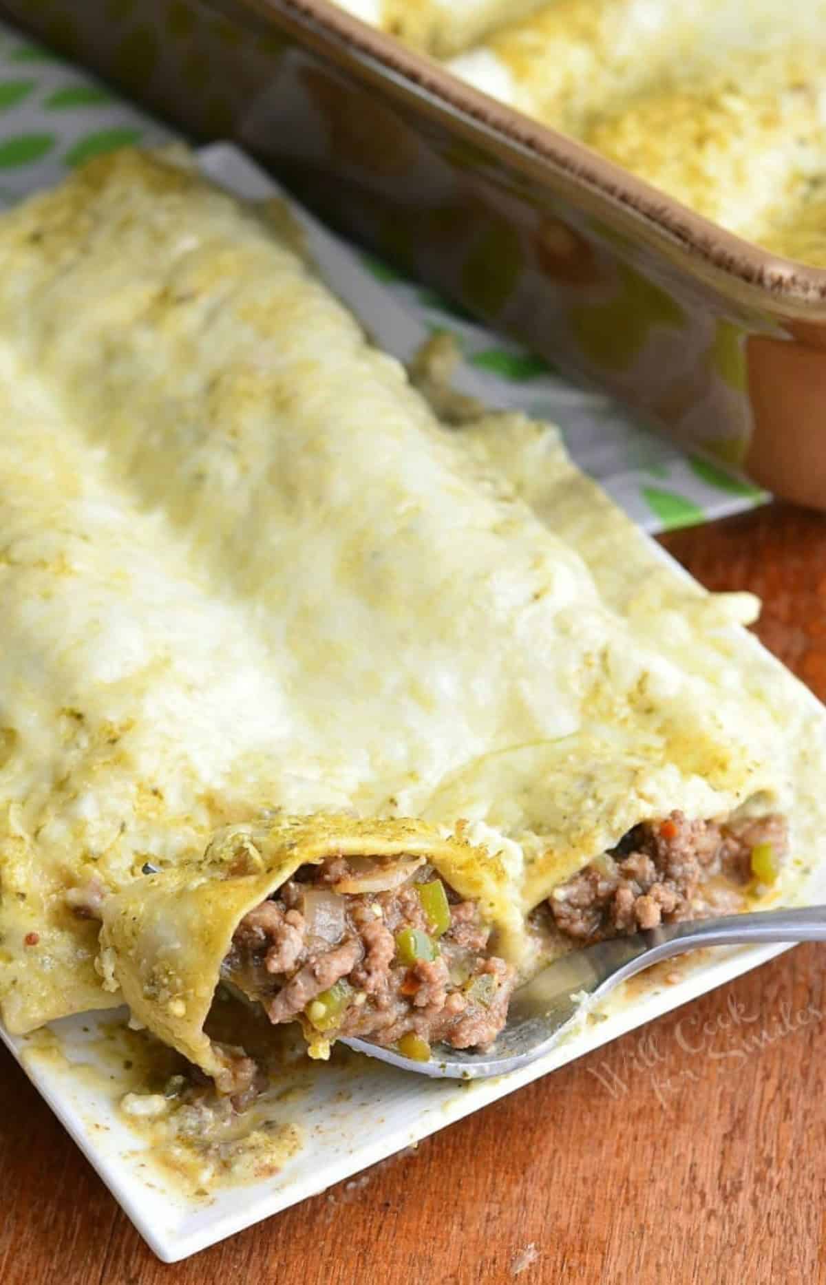 cutting a piece of beef enchilada with a fork on a plate next to the baking dish.