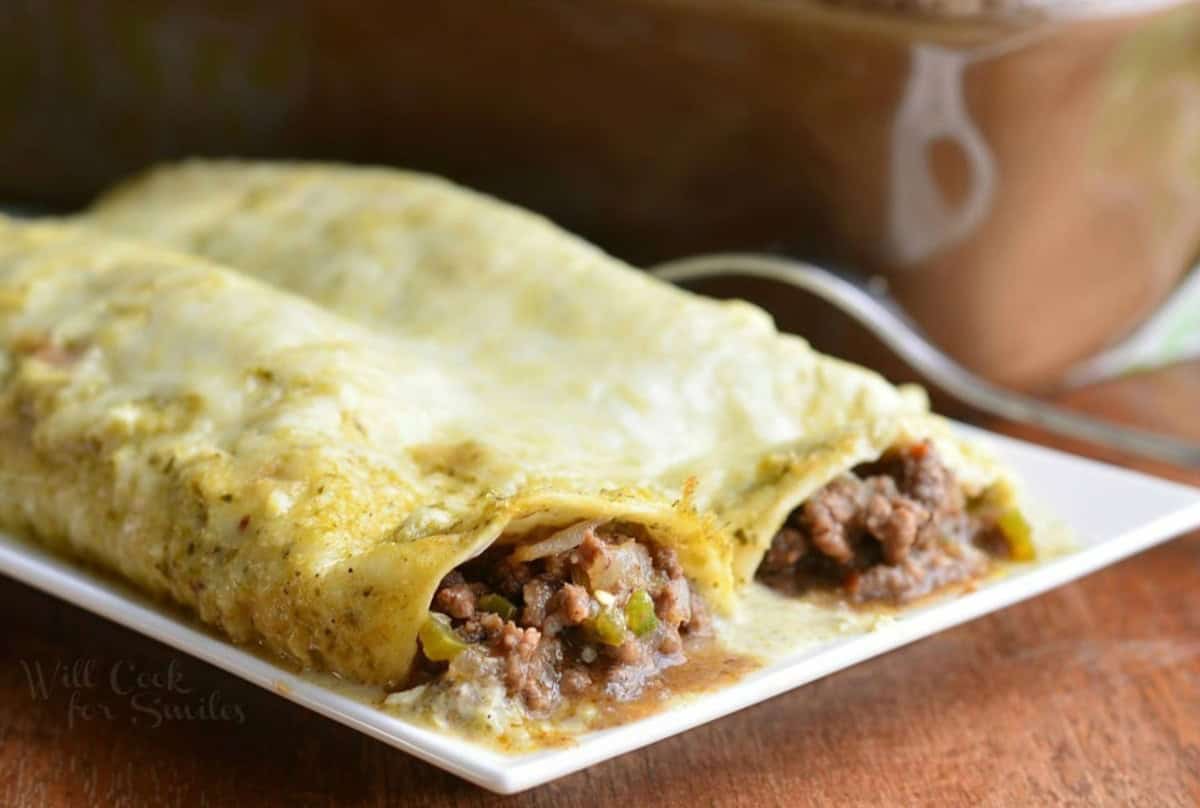 two beef enchiladas verdes in creamy sauce and cheese on a plate.