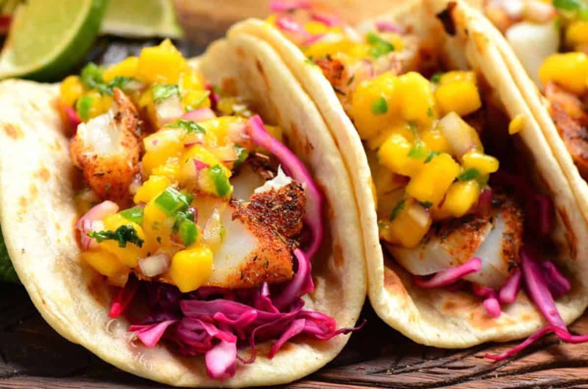 two fish tacos with mango salsa on top of them.