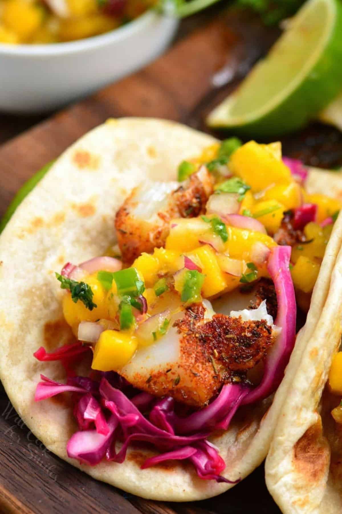 Blacked fish taco with cabbage and mango salsa on a wood surface.