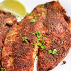 Blackened tilapia on a white plate with a slice of lime.