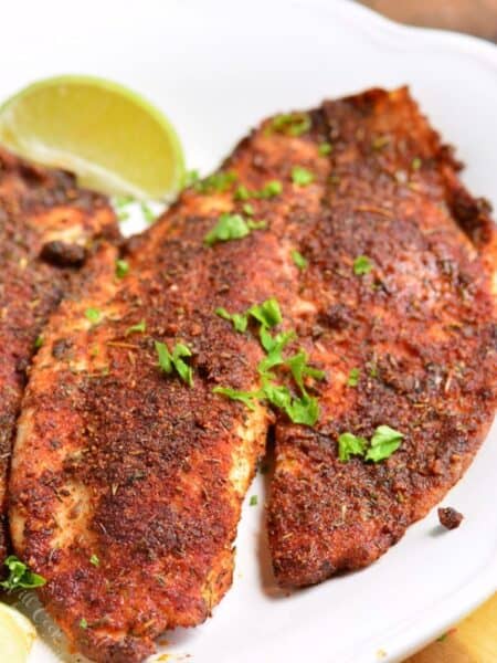 Blackened tilapia on a white plate with a slice of lime.