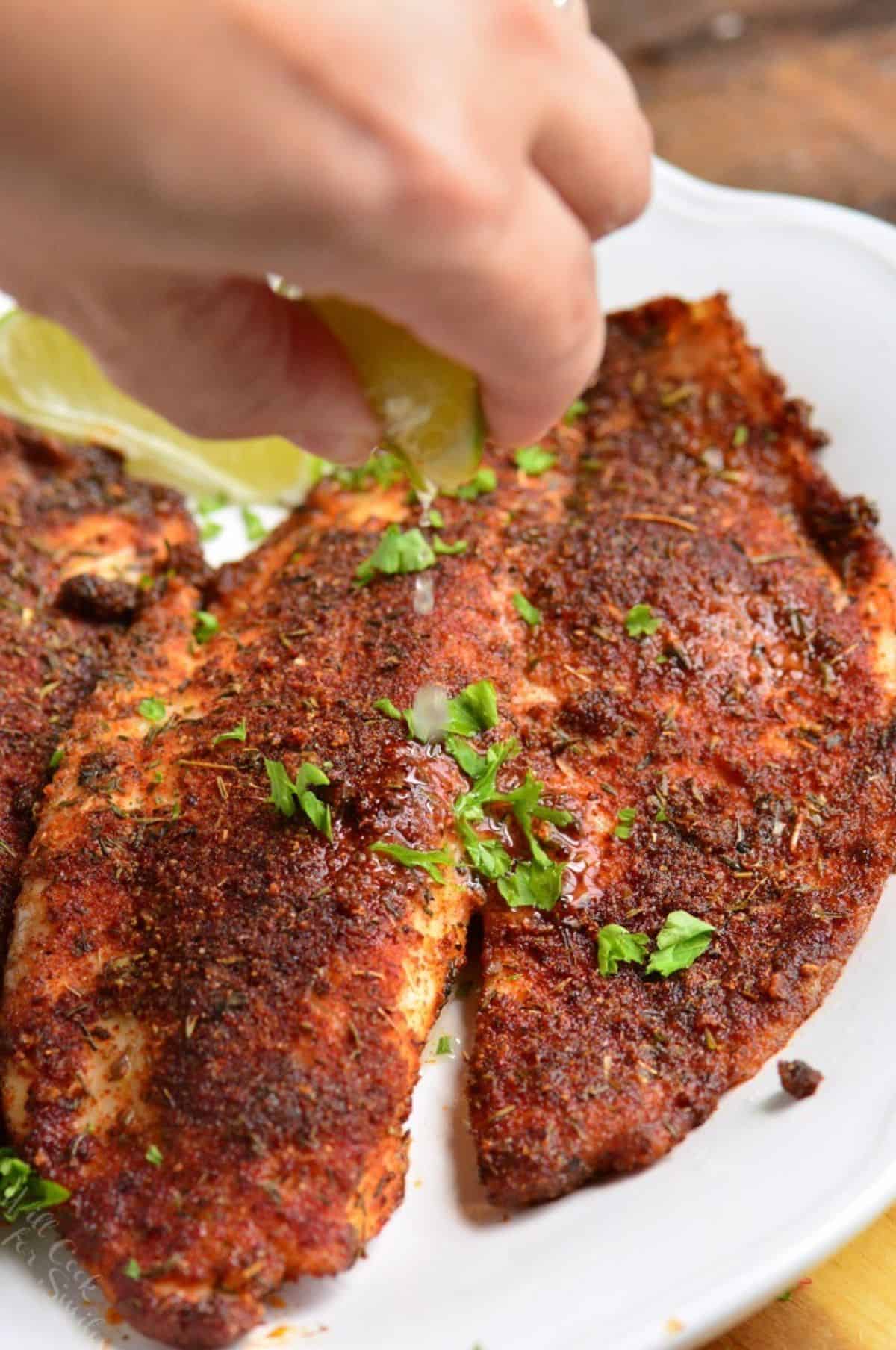 Squeezing lime over cooked blackened tilapia that is on a plate.