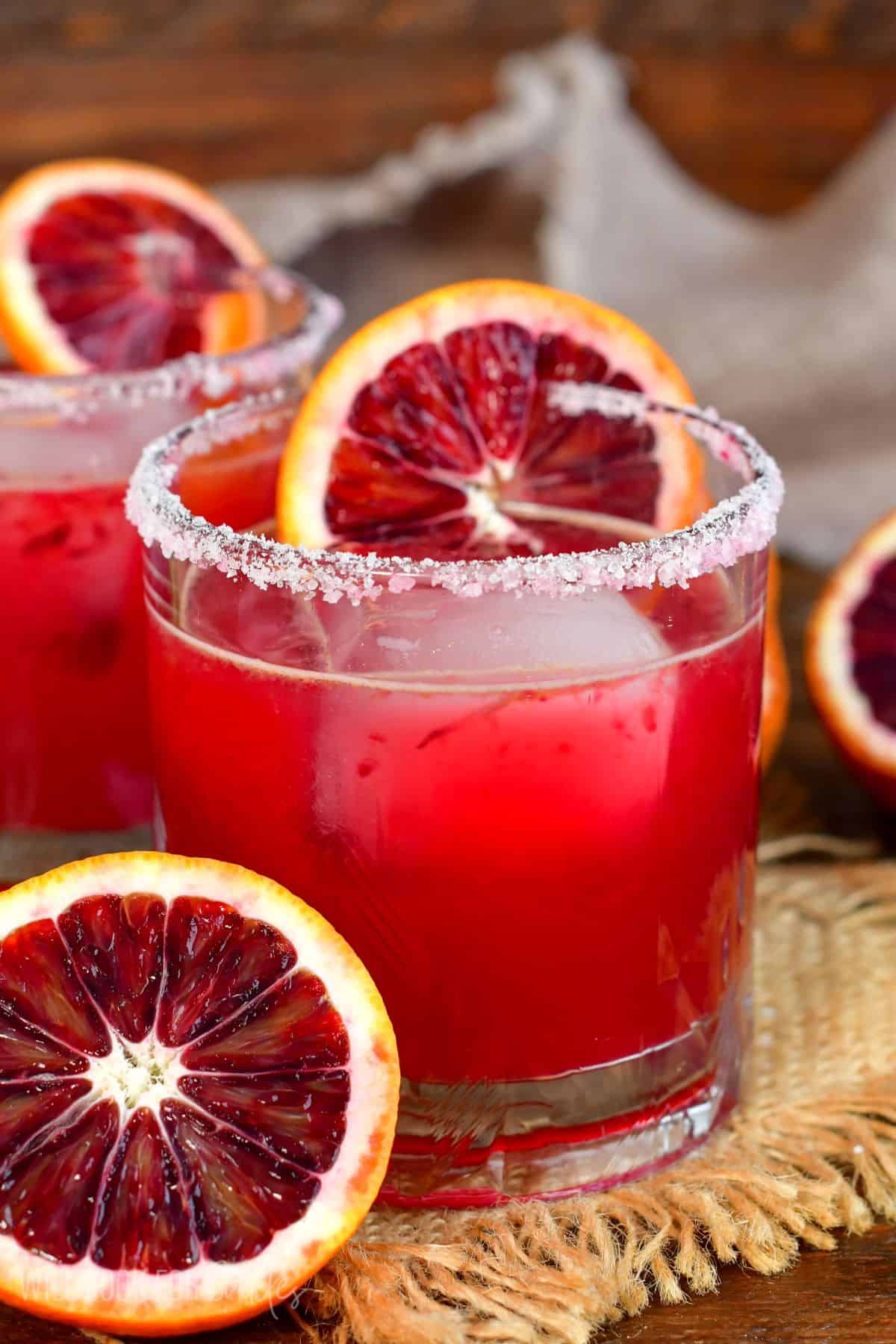 Blod orange margarita in a salt rimmed glass with a slice of orange on the glass as garnish and half an orange next to the glass.