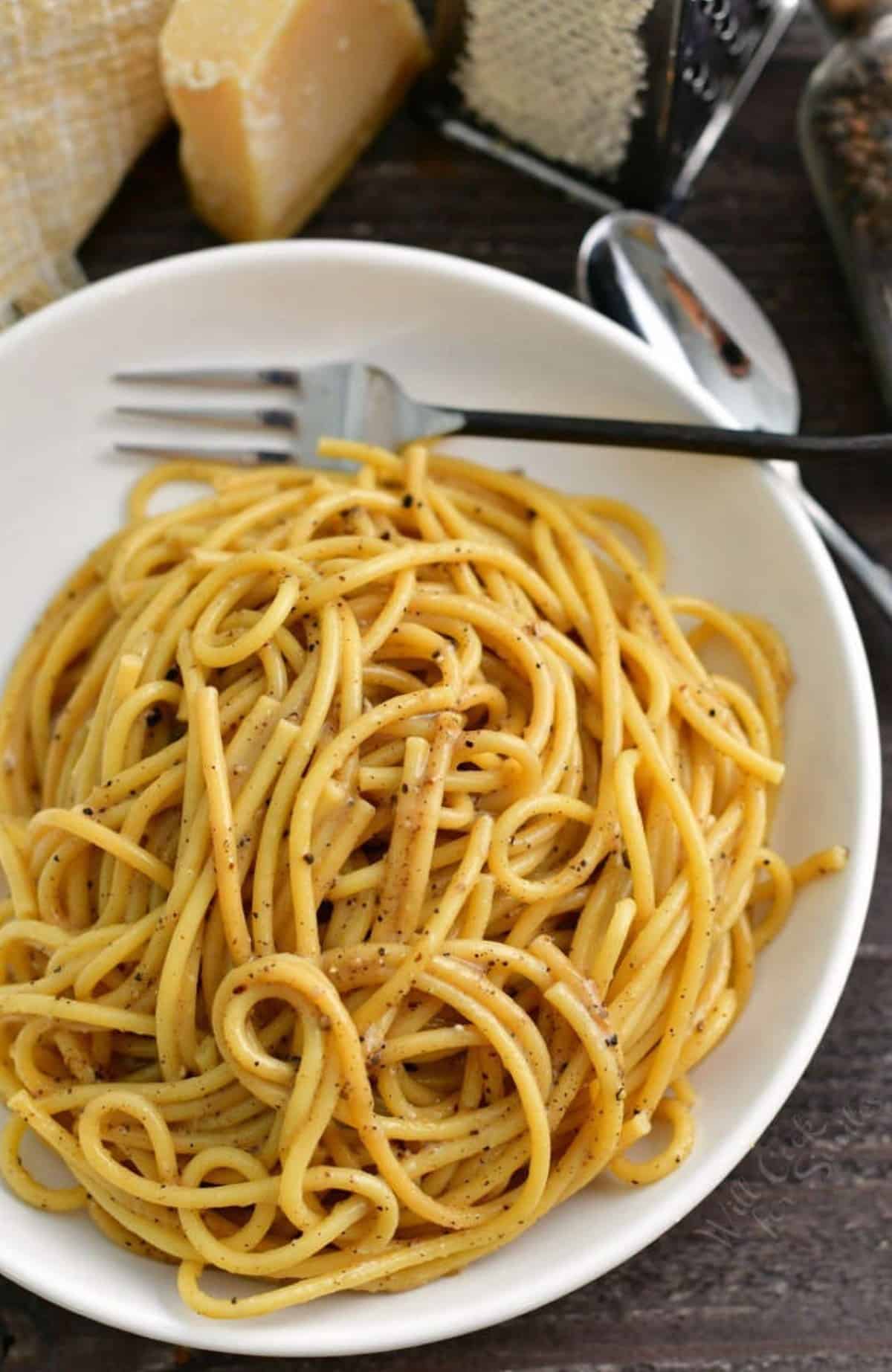 cacio e pepe pasta in a white bowl with fork on the edge.
