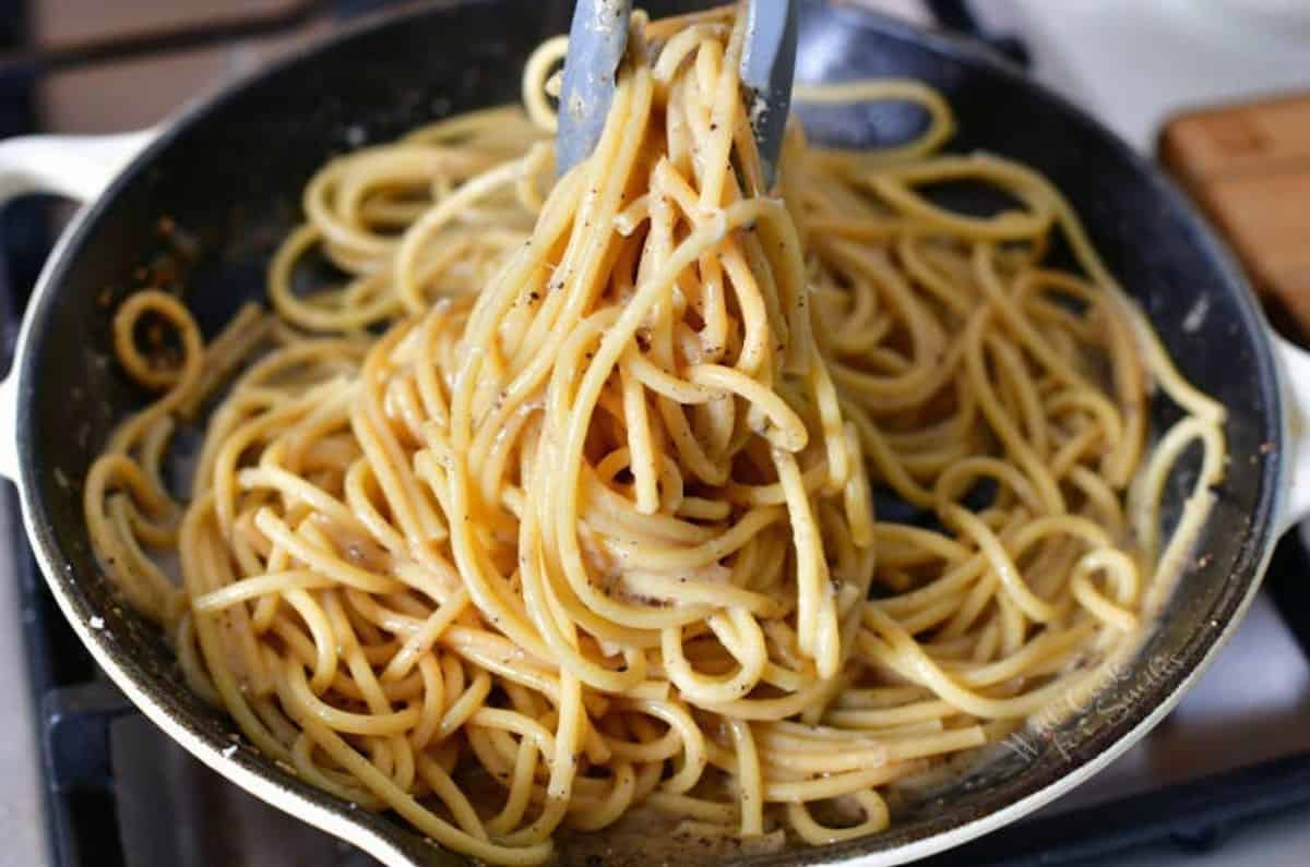 mixing the pasta with pepper cheesy sauce in the pan.