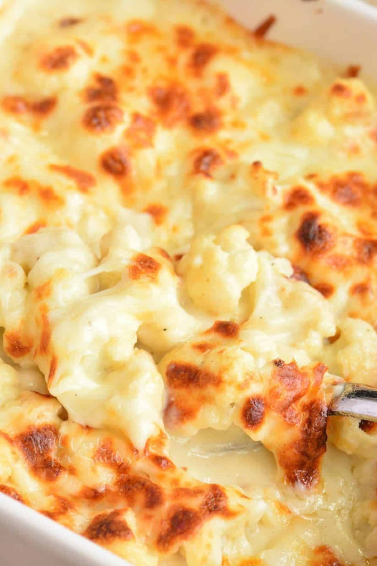 Scooping Cauliflower mac and cheese out of a baking dish.