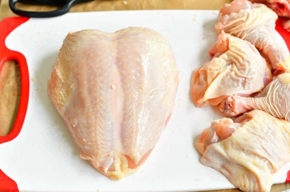 a whole chicken breast on a cutting board with the other peices to the side.