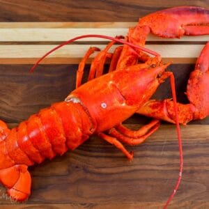 whole cooked lobster lain down on a wooden cutting board.