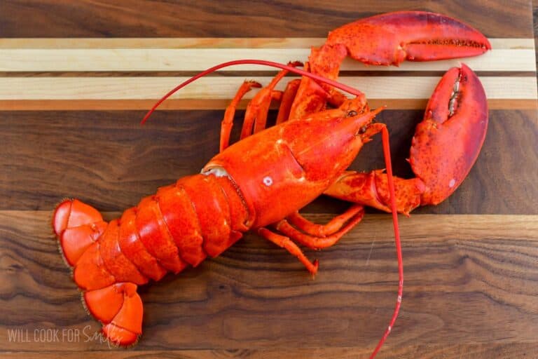 whole cooked lobster lain down on a wooden cutting board.
