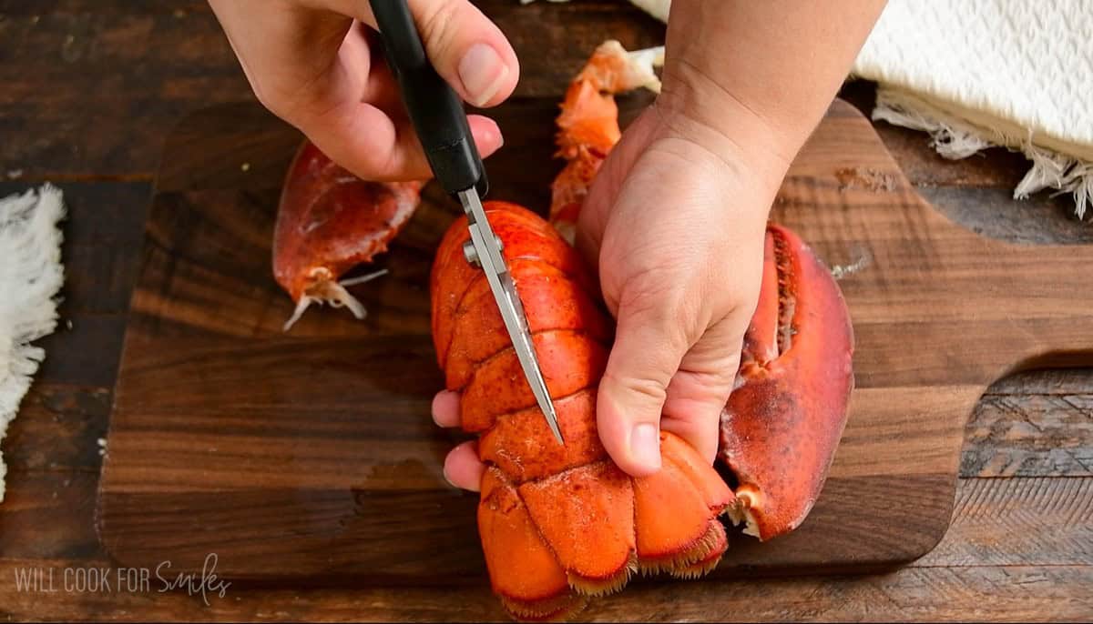 cutting through the cooked lobster tail with kitchen shears.