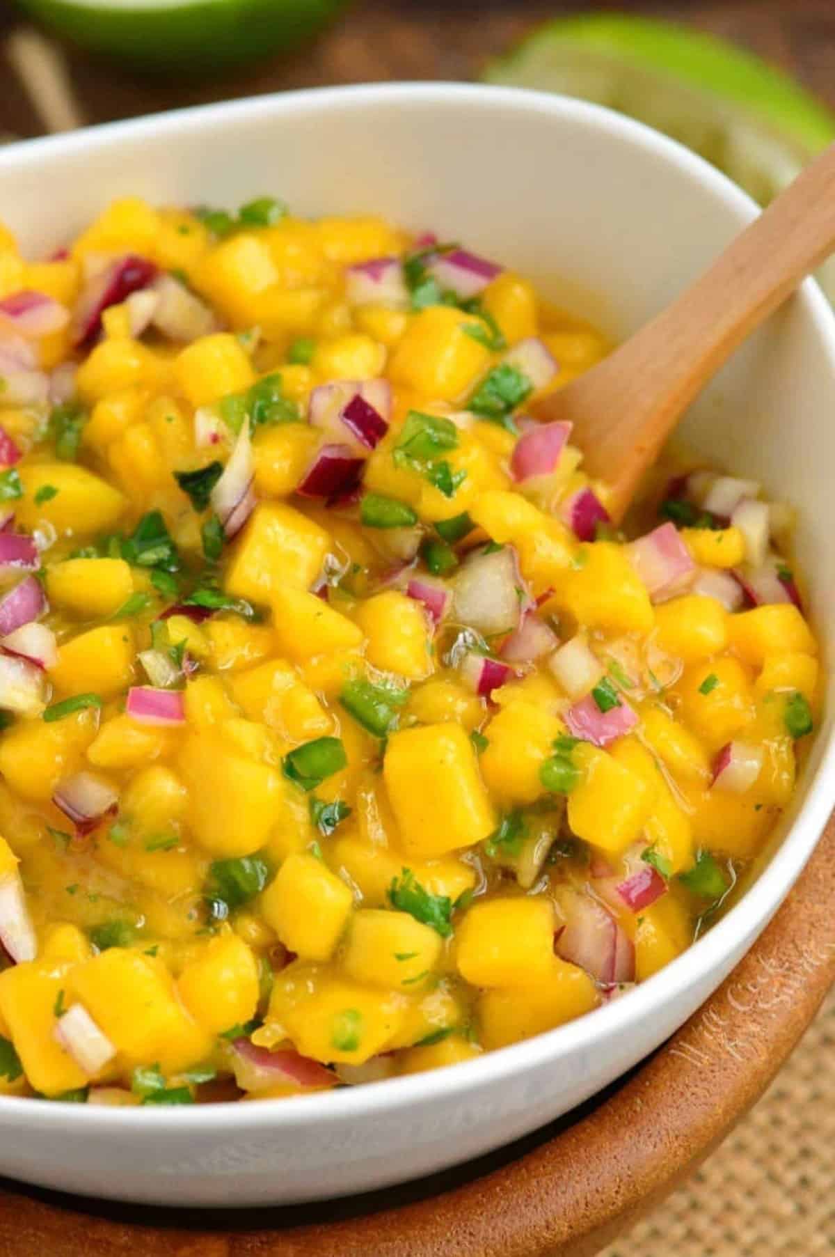 Mango salsa in a serving bowl with a wooden spoon.