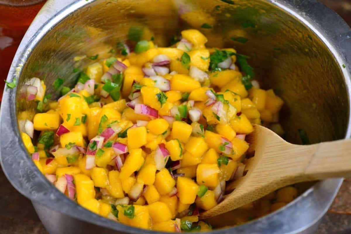 Mango salsa in a bowl being mixed with a wooden spoon.