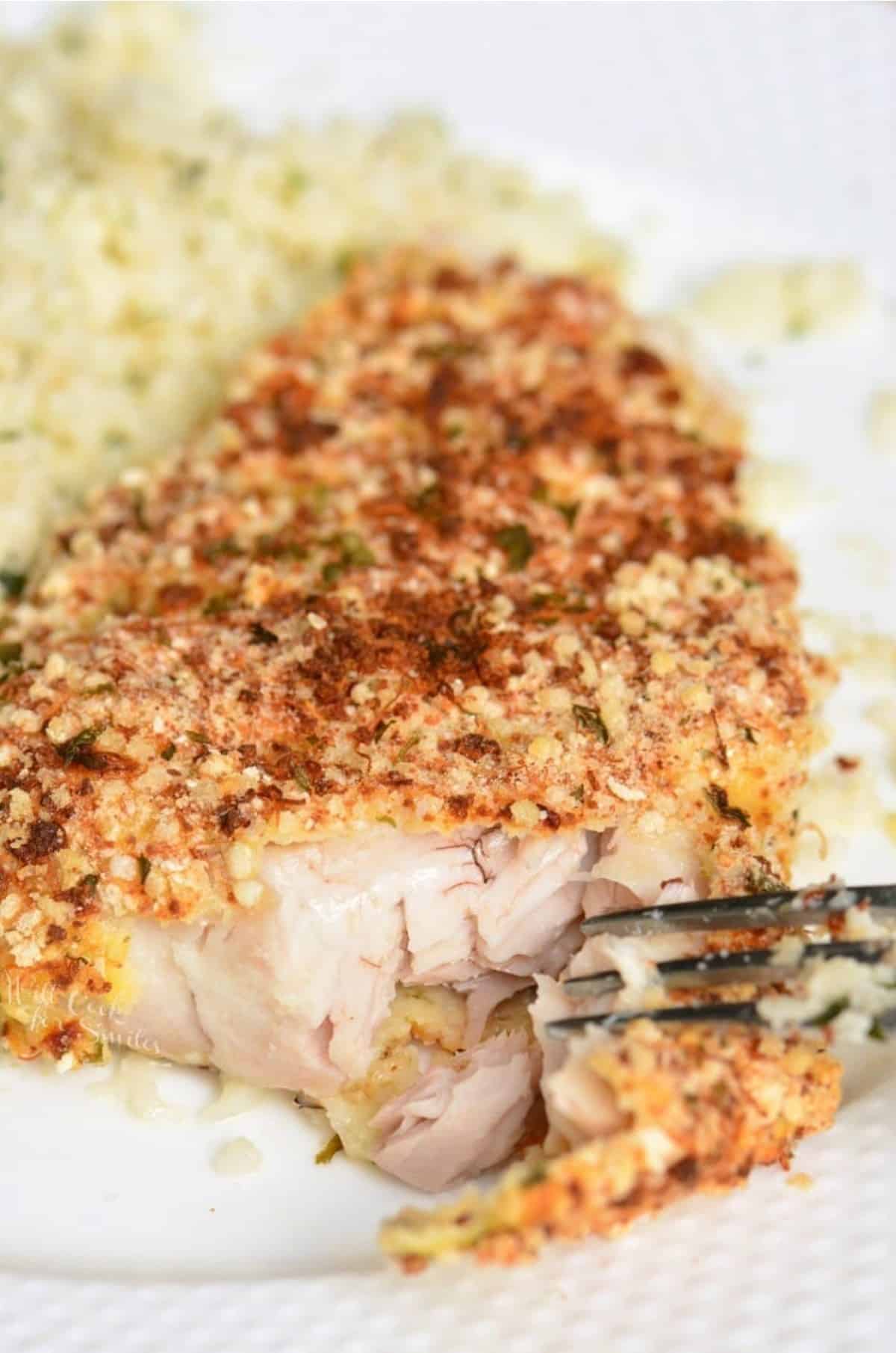 flaking off some mahi mahi off of the baked crusted filet on the plate.