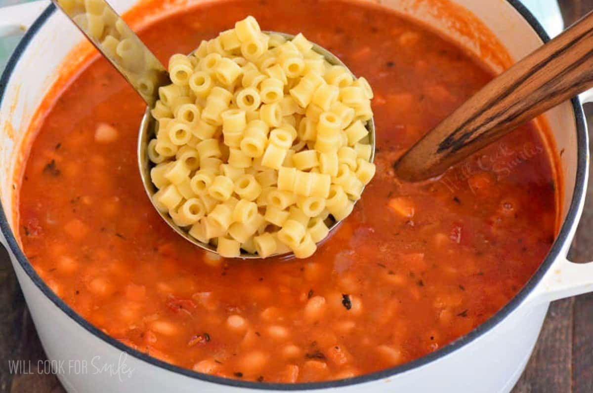adding ladlefuls of ditalini pasta to the pasta e fagioli soup.