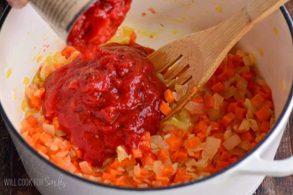 adding canned crushed tomatoes to the pot with sauteed veggies.